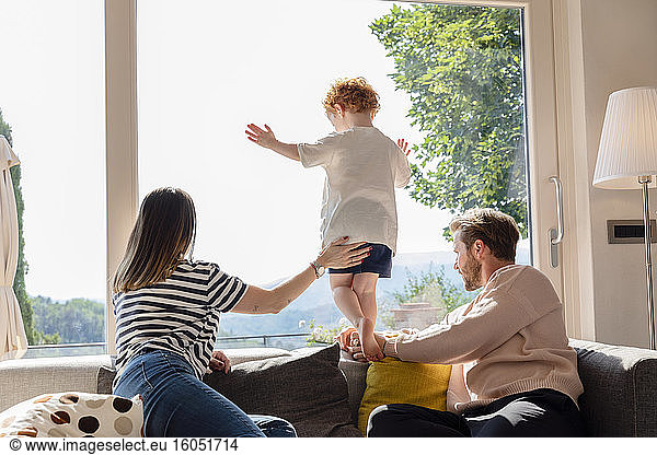 Parents and son looking out through window at home