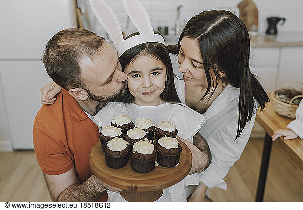 Parents embracing girl holding cupcakes at home