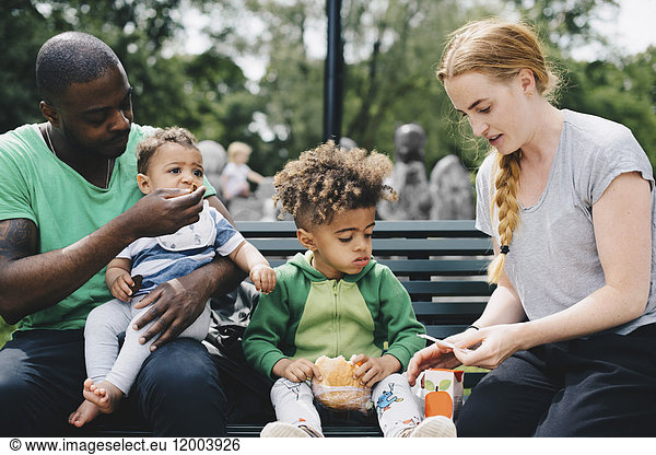 Parents having food with children while sitting on bench at park