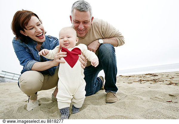 Parents helping baby walk on beach