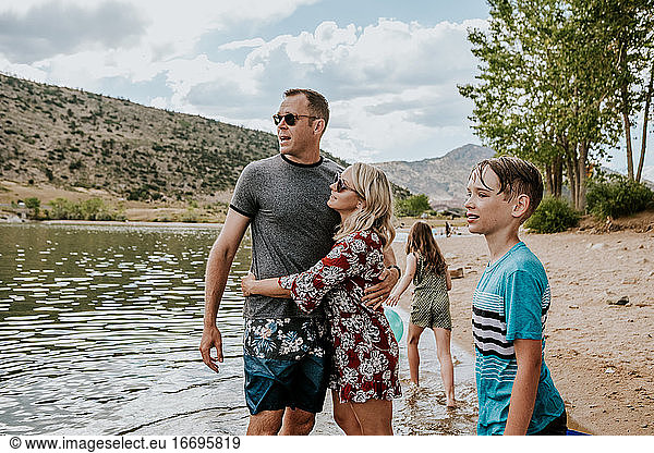 Parents hugging near a lake while their kids play
