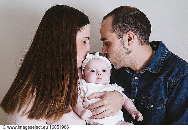 Parents kissing baby girl against wall at home