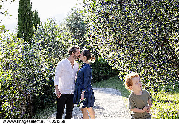 Parents kissing while cute boy playing at olive orchard