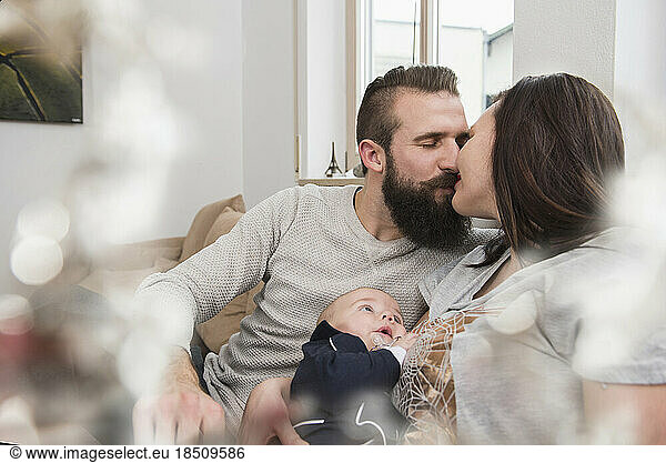 Parents kissing with baby on sofa