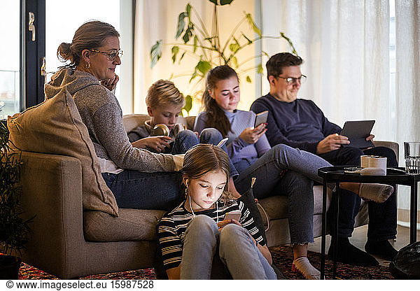 Parents sitting with children while using wireless technologies in living room at modern home