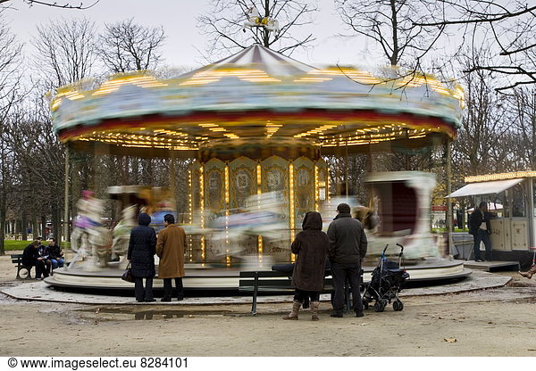 Parents watch their children on the carousel in Jardin des Tuileries  Central Paris  France