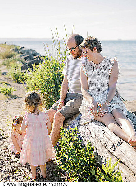 Parents watch while their playful twin girls explore the sandy beach