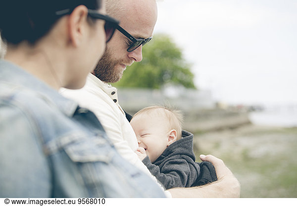 Parents wearing sunglasses holding little baby outdoors