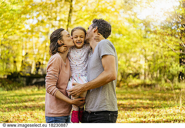 Parents with eyes closed kissing daughter in park
