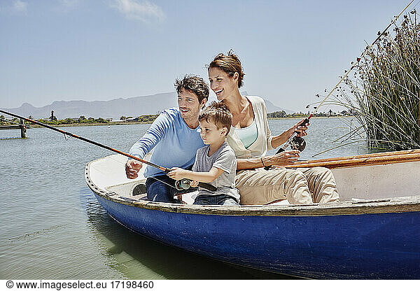 Parents with fishing rod sitting by son in rowboat on lake