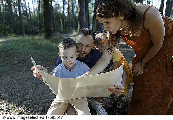 Parents with son and daughter reading map in forest