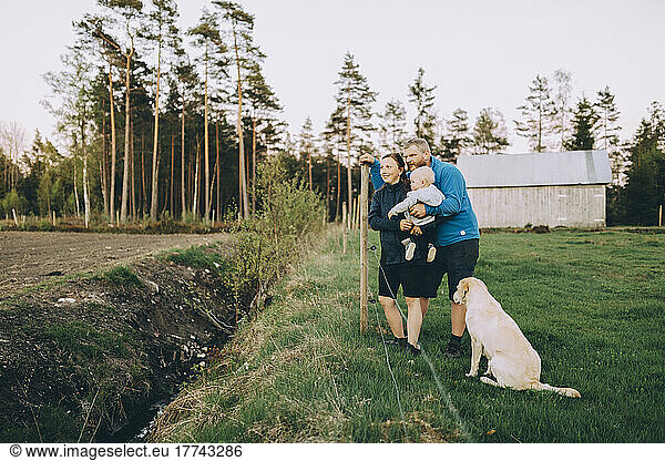 Parents with son and pet dog standing in farm during sunset