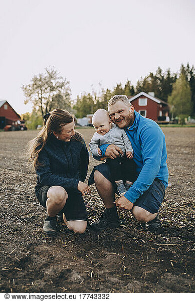 Parents with toddler son crouching at farm during sunset