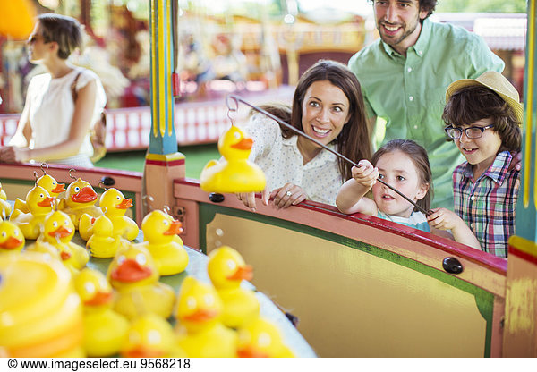 Parents with two children having fun with fishing game in amusement park