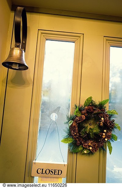 Parte trasera de una puerta con el cartel de 'CLOSED' colgado  una corona navideña  y una campana en una tienda de antigüedades. Skipton  North Yorkshire  UK.
