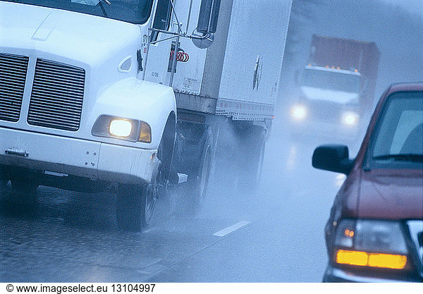 Partial view of large commercial truck driving in hazardous conditions of snow and rain on a freeway.