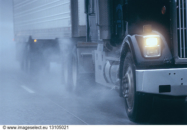Partial view of large commercial truck driving in hazardous conditions of snow and rain on a freeway.