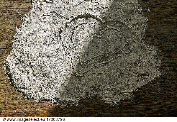 Partly shadowed heart drawn by finger in flour on cutting board