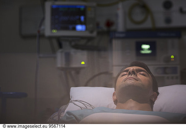 Patient lying in bed  surrounded by monitoring medical equipment in intensive care unit
