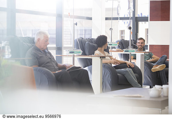 Patients in armchairs receiving medical treatment in hospital ward