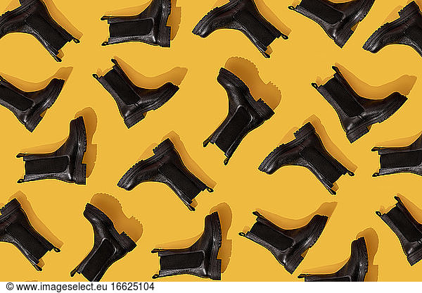 Pattern of black leather boots against yellow background