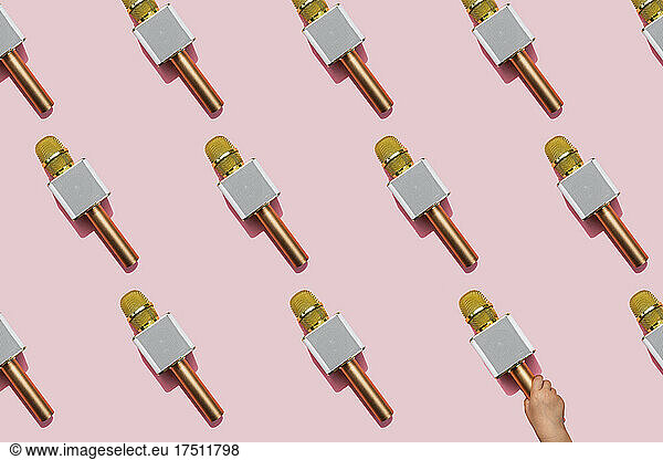 Pattern of golden microphones against pink background with hand of baby girl picking one up