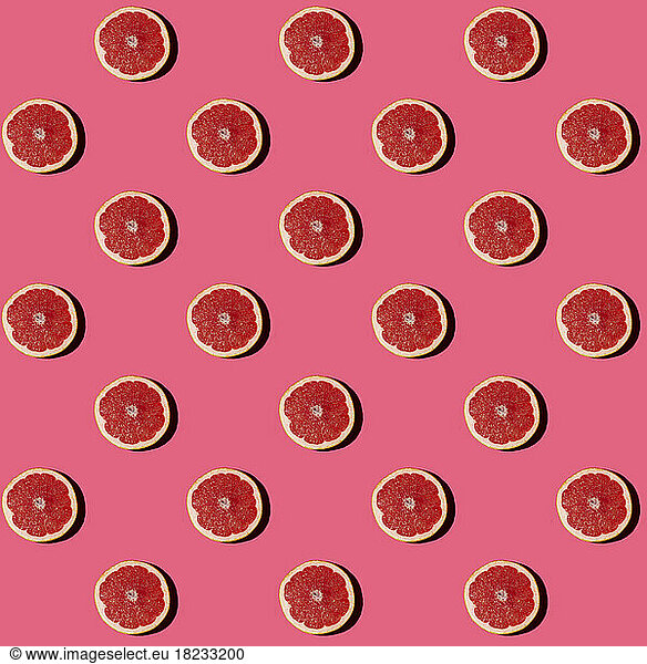 Pattern of halved grapefruits flat laid against pink background