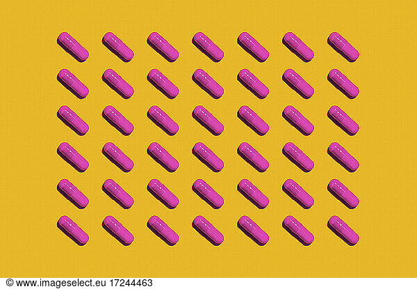 Pattern of rows of pink medicine capsules laid against yellow background