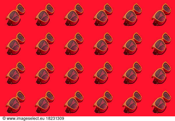 Pattern of rows of retro styled sunglasses flat laid against red background