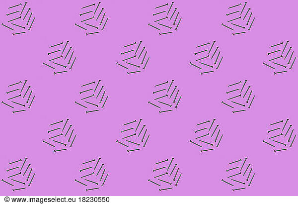 Pattern of rows of screws flat laid against pink background