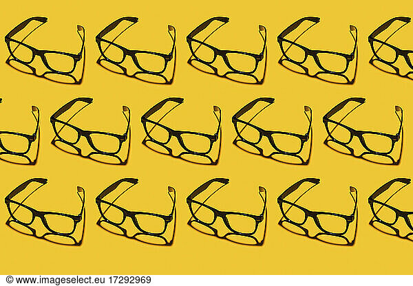 Pattern of rows of simple classic eyeglasses flat laid against yellow background