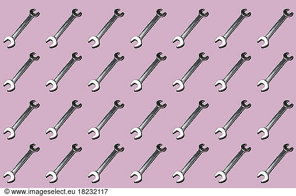 Pattern of rows of wrenches flat laid against pink background