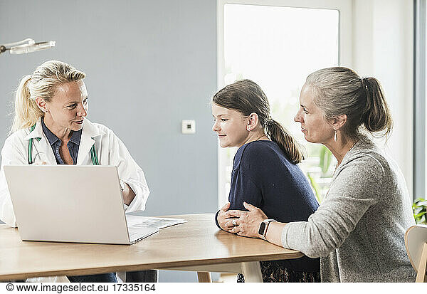Pediatrician explaining patient and woman with laptop at doctor's office