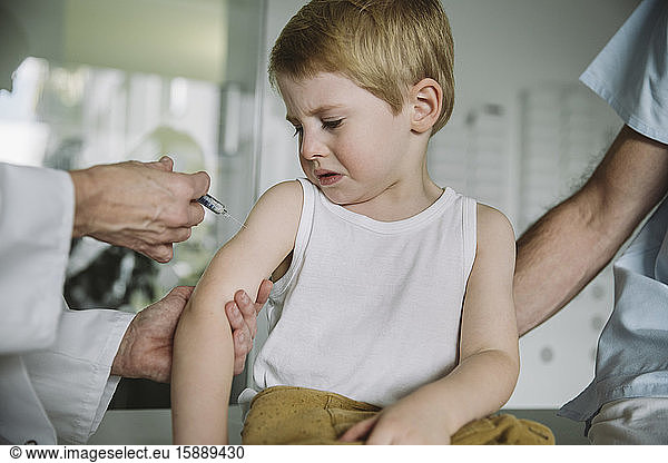 Pediatrist injecting vaccine into arm of unhappy toddler