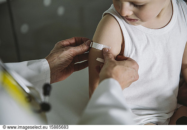 Pediatrist putting band-aid onto arm of toddler after vaccination