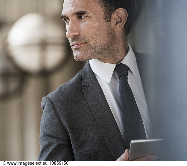 Pensive corporate businessman with digital tablet looking away