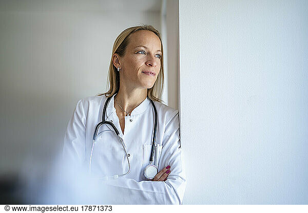 Pensive female doctor leaning against a wall