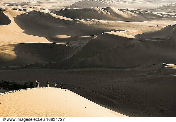 People climbing sand dunes to watch the sunset over the desert at Huacachina  Ica Region  Peru