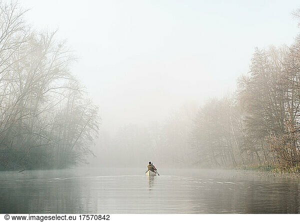 People in a canoe boat paddling away on the misty tranquil river