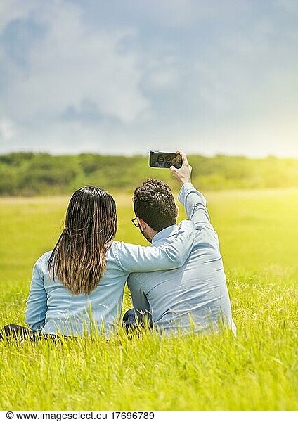 People in love taking selfies in the field with their smartphone  Smiling couple in love sitting on the grass taking selfies  Young couple in love taking a selfie in the field