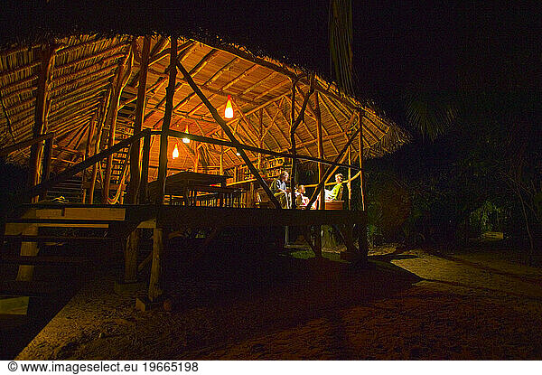 People relaxing inside an open-air Caribbean resort bungalow.