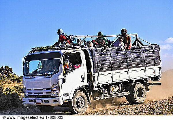People stand in the back of a truck travelling down a dusty dirt road in rural Ethiopia; Ethiopia
