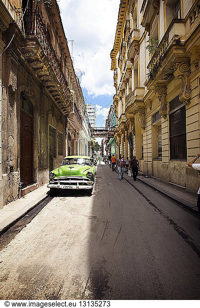 People walking by vintage car parked on street amidst buildings