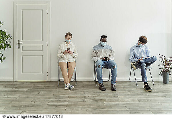 People wearing face masks sitting on chairs in waiting area