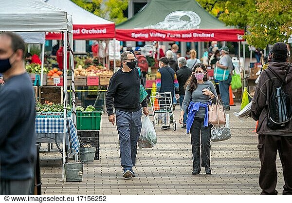 People wearing masks walk around plaza of Silver Spring Farmers Market   Silver Spring  MD.