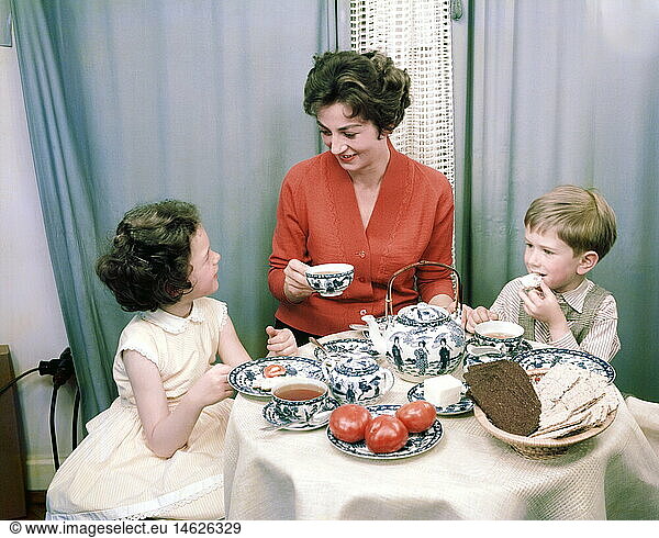 people  woman with child  mother with daughter and son sitting at dining table  circa 1960