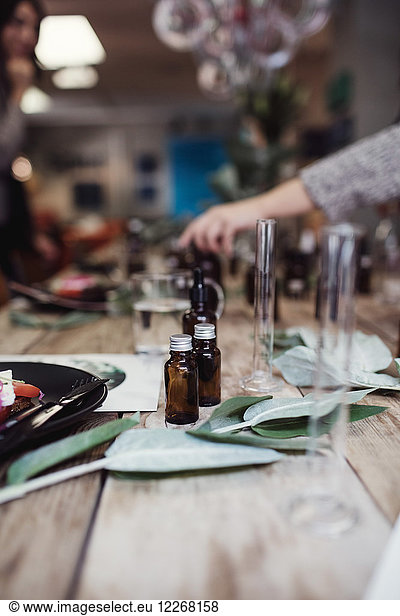 Perfume bottles by leaves and plate on table at workshop