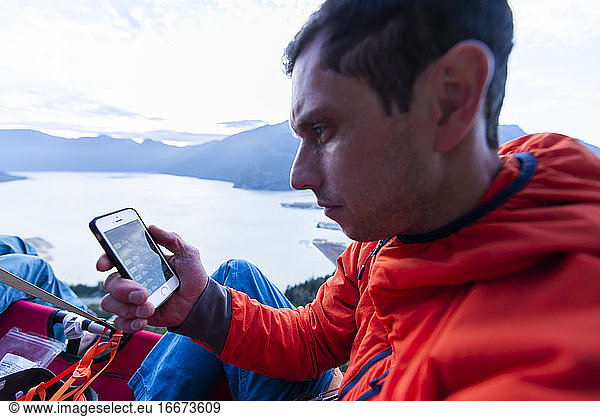 Perplex man looking at phone sitting on portaledge at sunset thinking