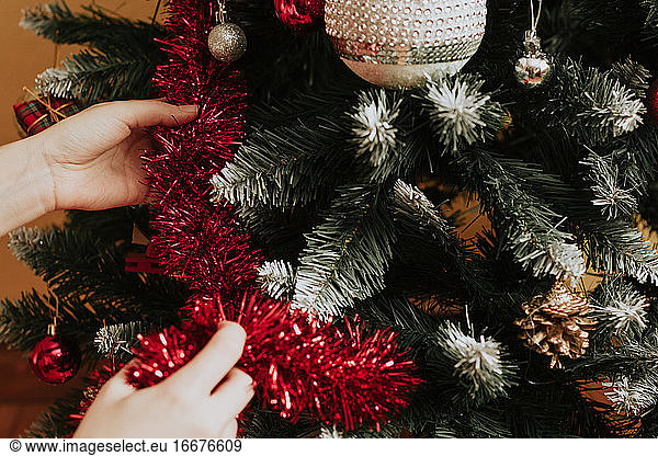 Person  die einen Nadelbaum am ersten Weihnachtstag mit rotem Lametta schmückt