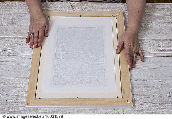 Person fitting a picture frame around a print.